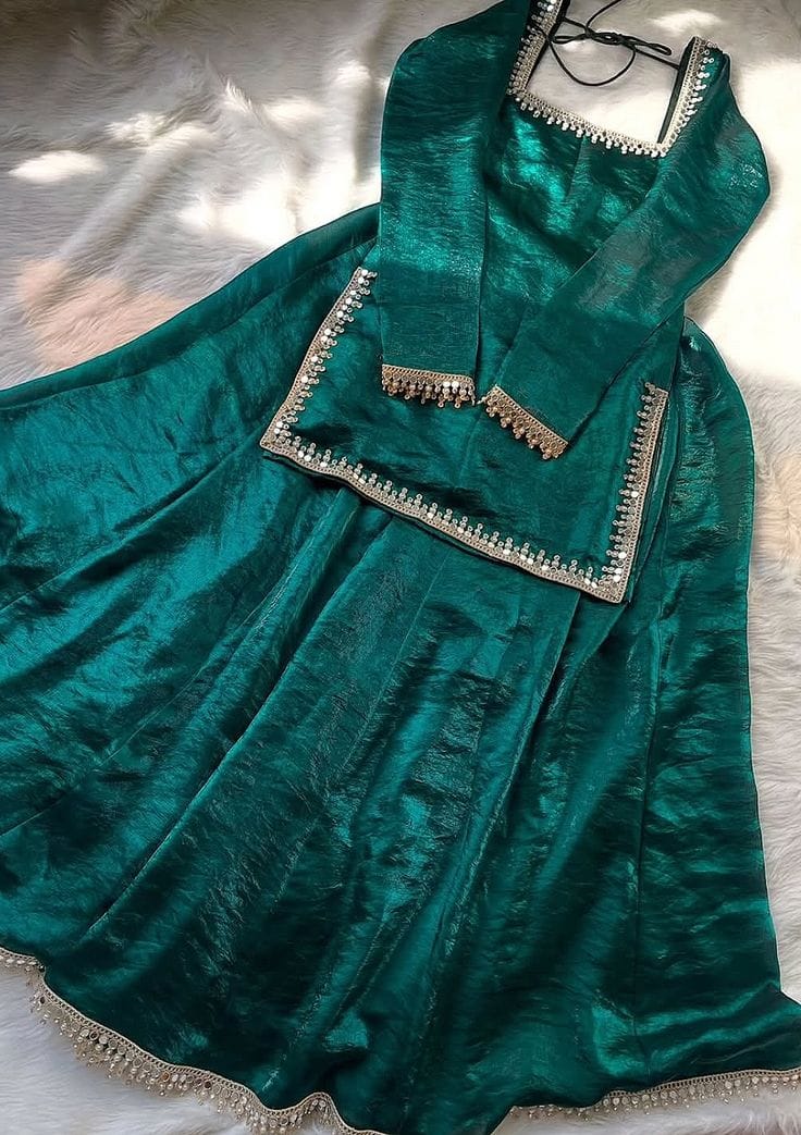 Flat lay of a luxurious white or ivory sheer organza kurta set with heavy silver mirror work (Shisha/Abla) trim along the square neckline, front opening, and hemline. The ensemble includes a matching dupatta and sleeve cuffs, laid out on a soft white surface.